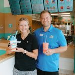 Elizabeth and Chris Reberk, owners of the Bahama Buck's in Inlet Beach, smile for a photo while standing behind the counter of their shop. Elizabeth holds a blue shaved ice and Chris holds an orange smoothie.
