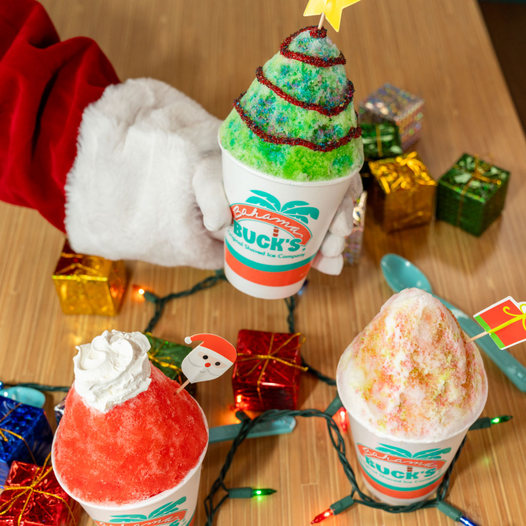 A Santa hand is shown holding a Christmas Tree Sno next to Santa and Christmas Cookie Snos on a festive table.